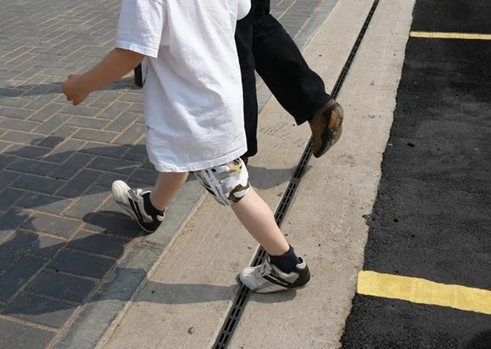 Persona caminando junto a una línea de drenaje en el pavimento